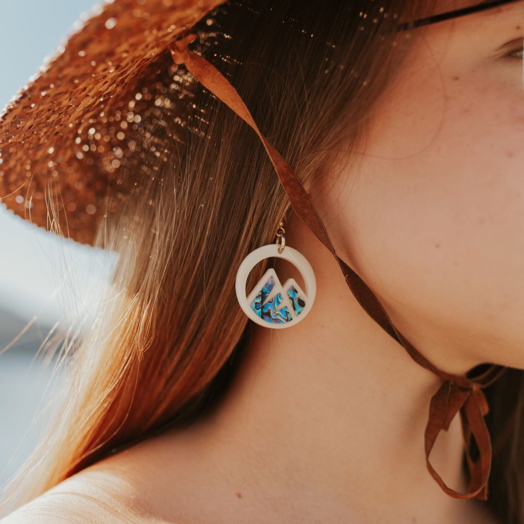 close up of young woman wearing ivory acrylic earring with mountain cut out and abalone inlay from copper canoe woman