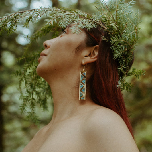 woman wearing gold mirror long rectangle warrior spirit earring with triangle zig zag abalone inlay from copper canoe woman