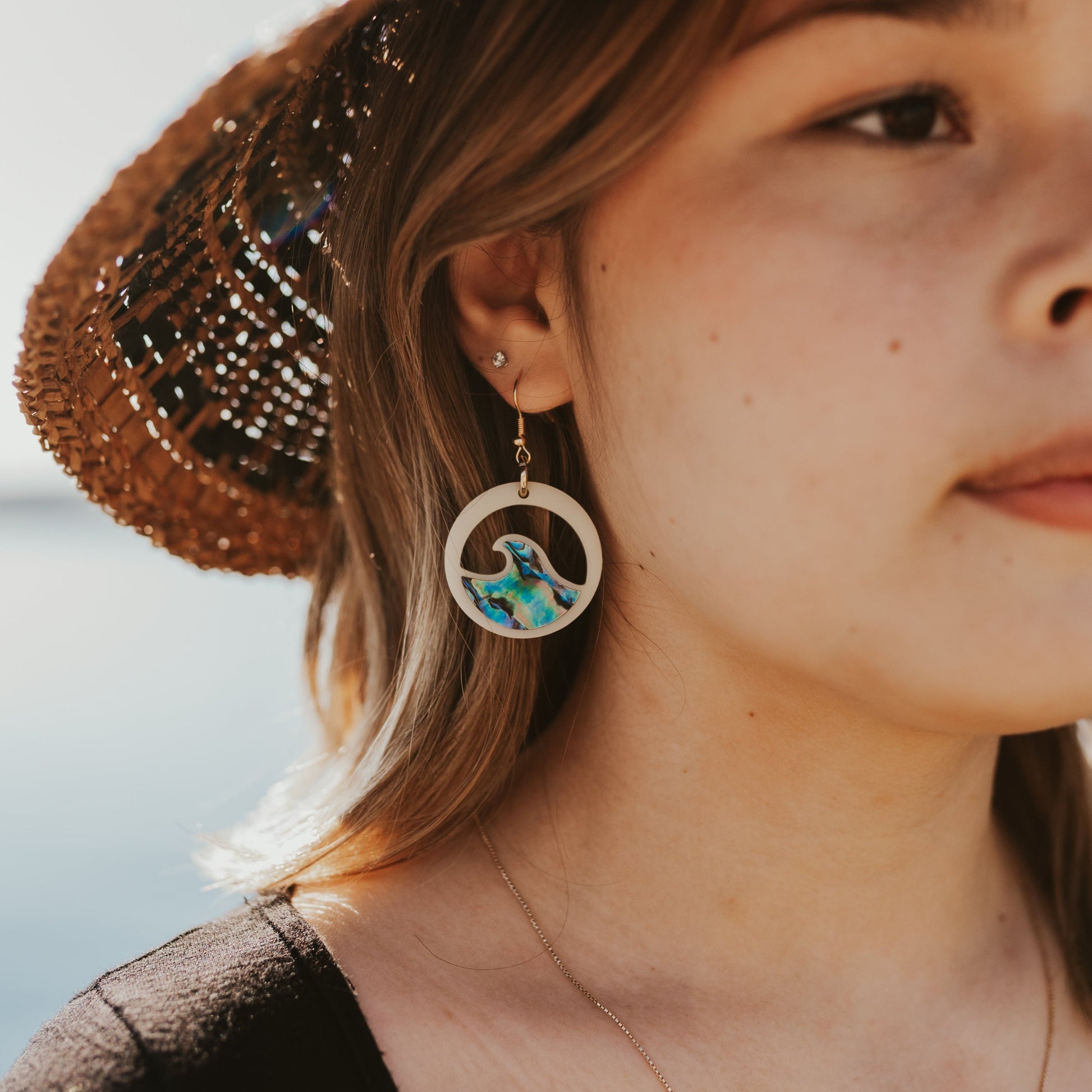 young woman wearing ivory acrylic earring with wave cut out and abalone inlay from copper canoe woman