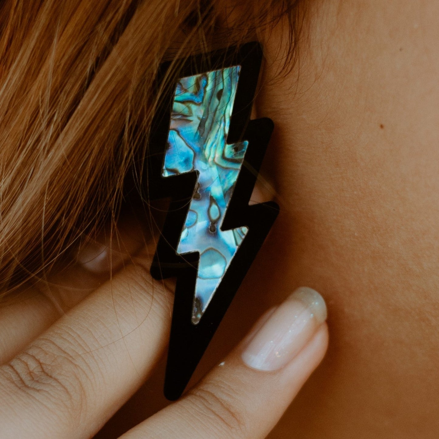 Closeup of model wearing lightning bolt earrings in black acrylic from Copper Canoe Woman.