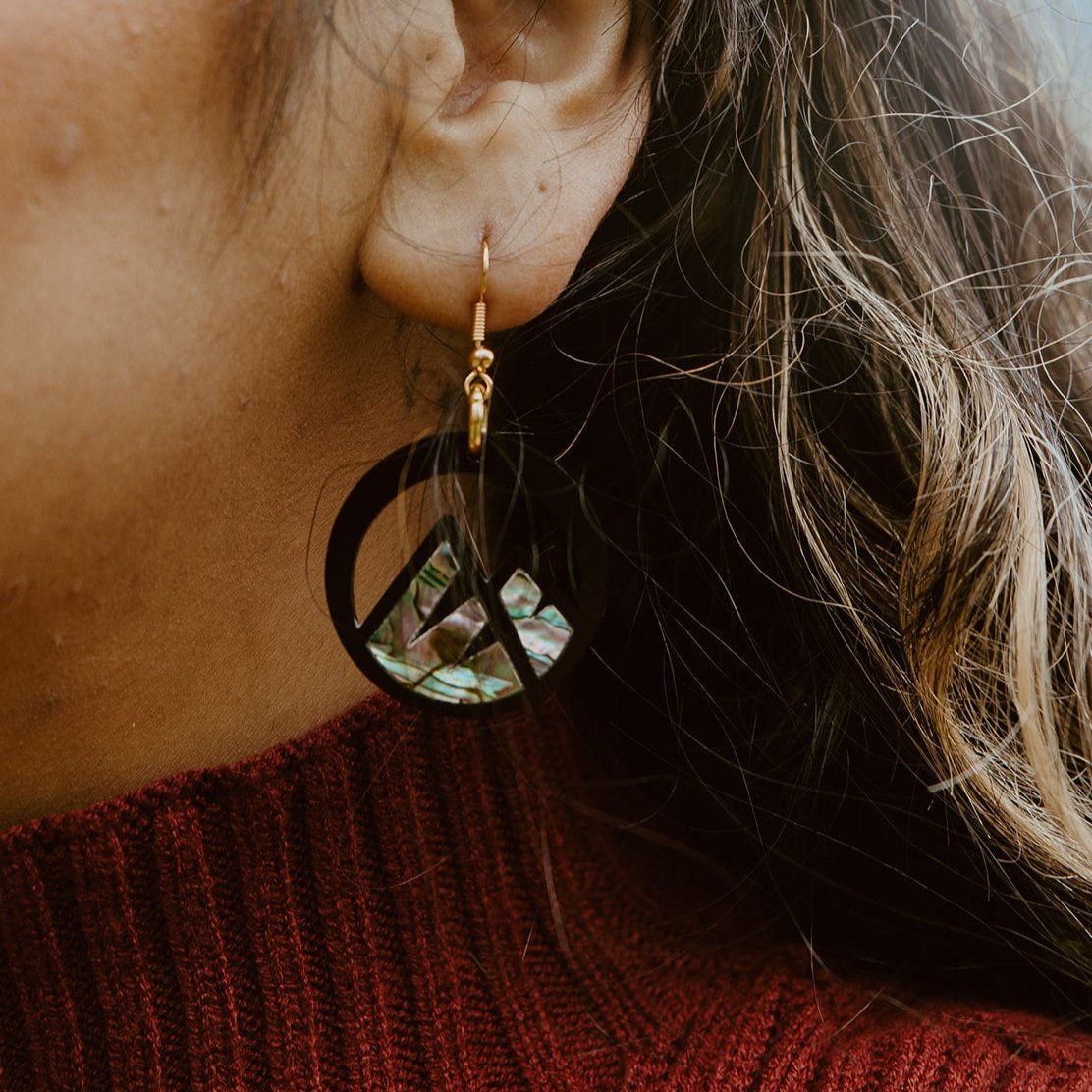 close up of woman wearing black acrylic earring with mountain cut out and abalone inlay from copper canoe woman