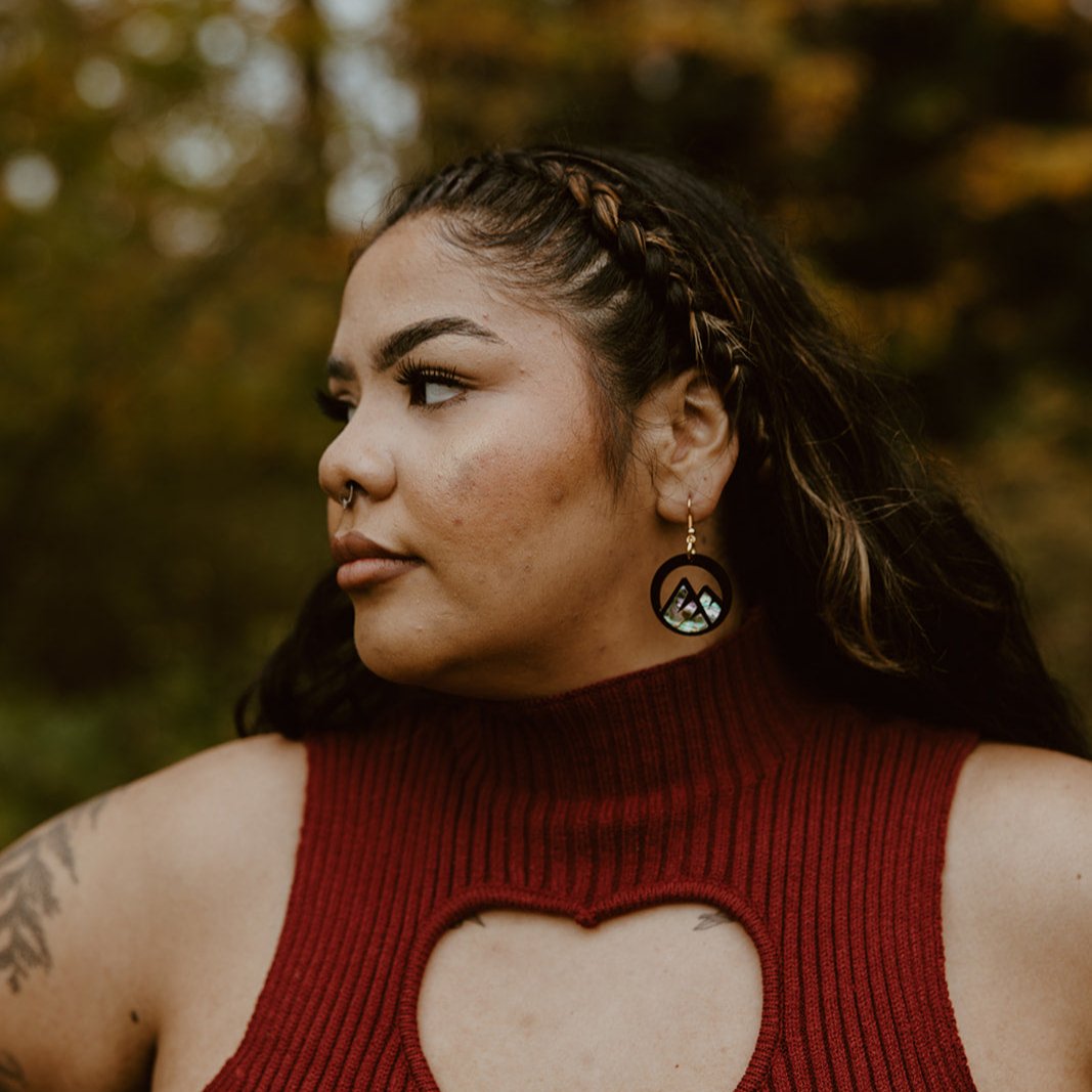  woman wearing black acrylic earring with mountain cut out and abalone inlay from copper canoe woman