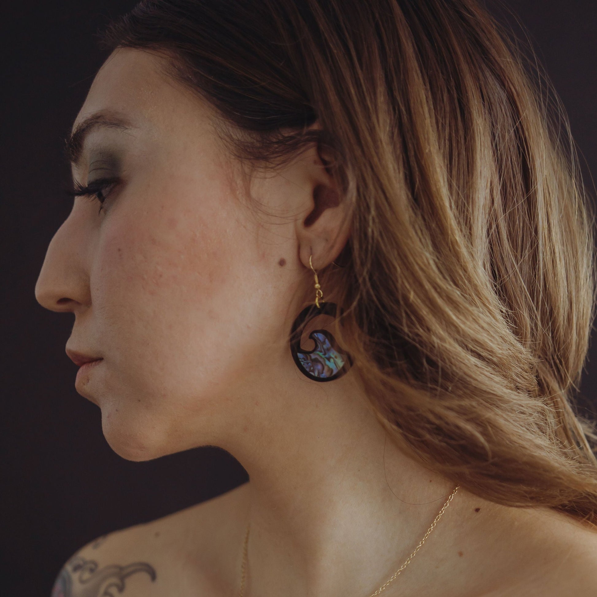 woman wearing black acrylic earring with wave cut out and abalone inlay from copper canoe woman