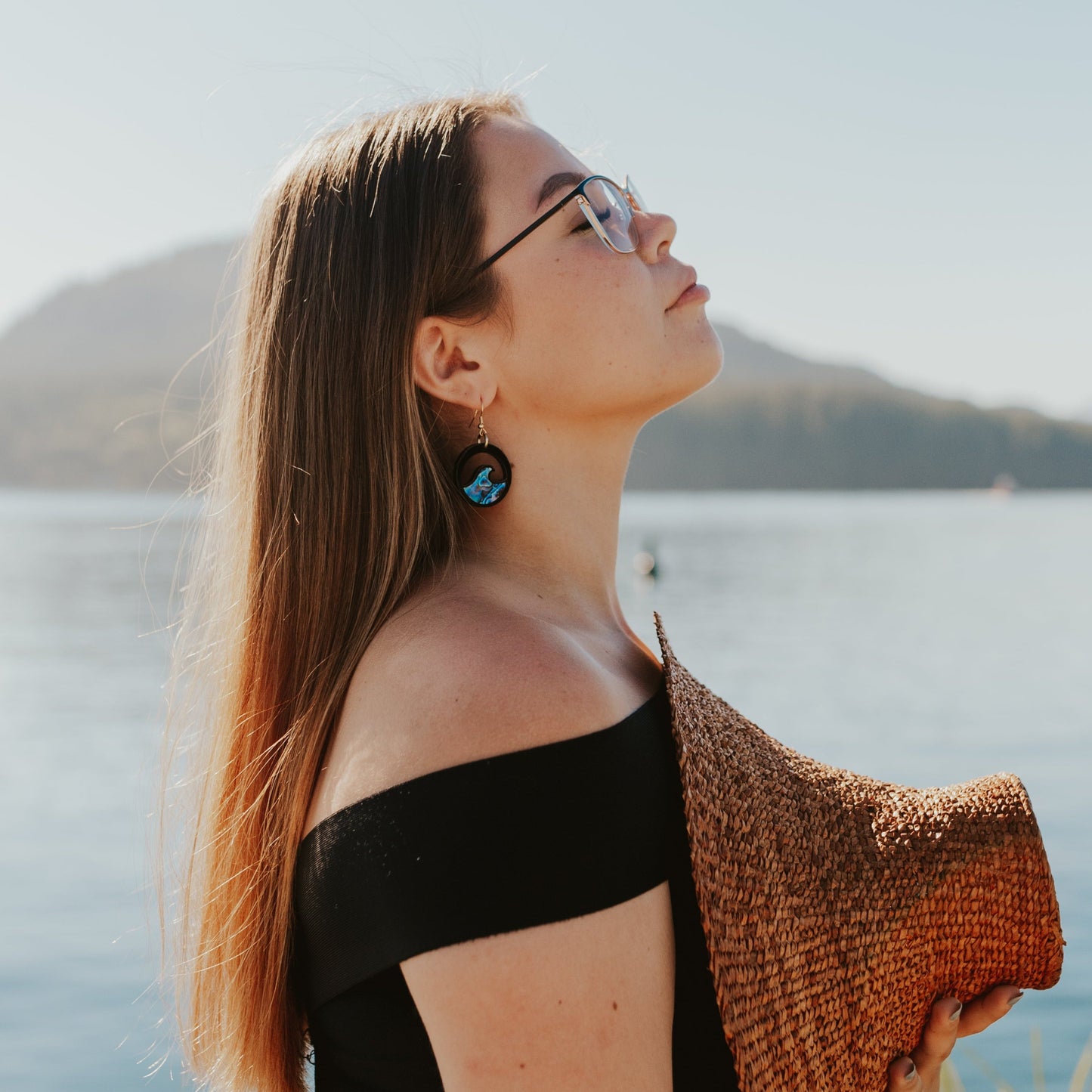 young woman wearing black acrylic earring with wave cut out and abalone inlay from copper canoe woman