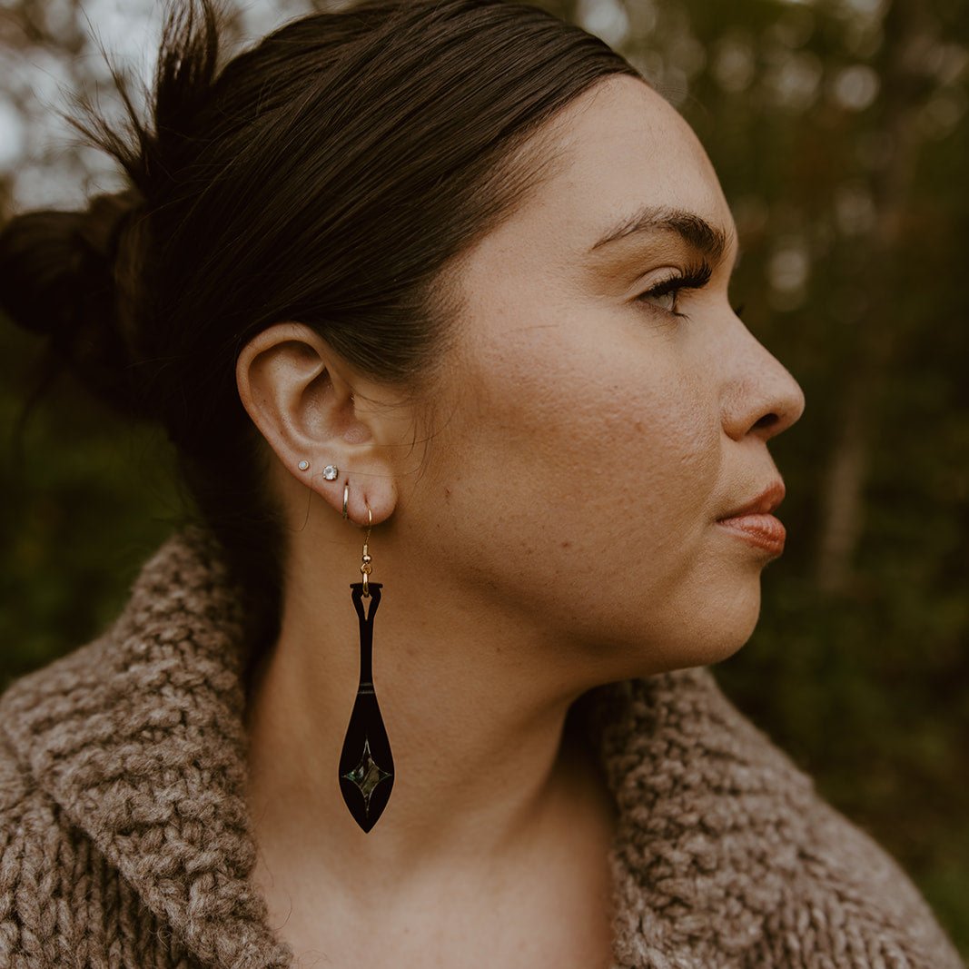 close up woman wearing black acrylic paddle earring with star abalone inlay from copper canoe woman