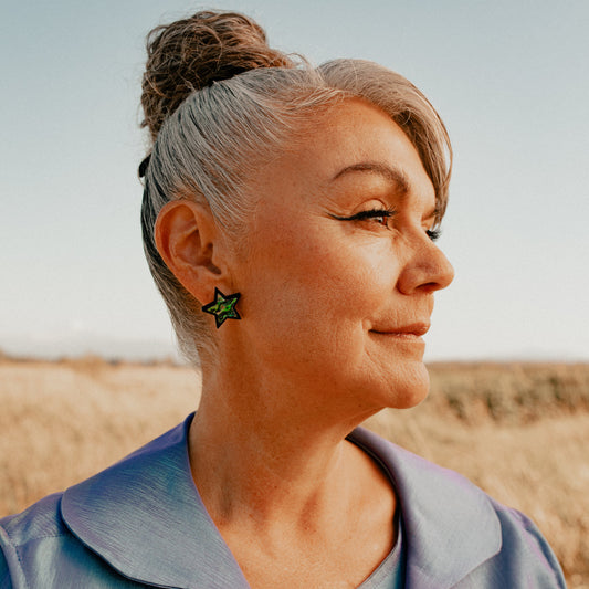 A model in profile wears the "Bright Star" earring from Copper Canoe Woman in black acrylic and abalone inlay.