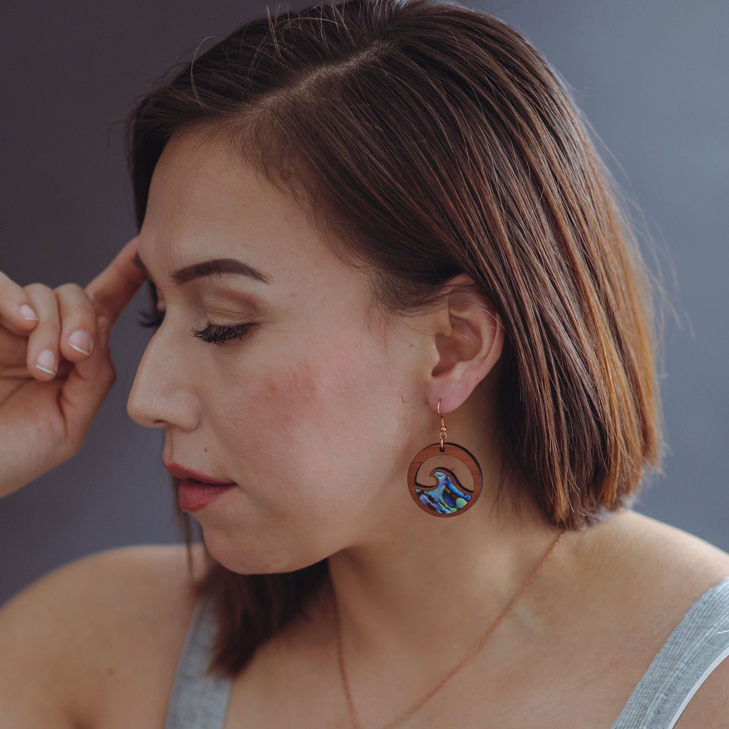 woman wearing cedar earring with wave cut out and abalone inlay from copper canoe woman