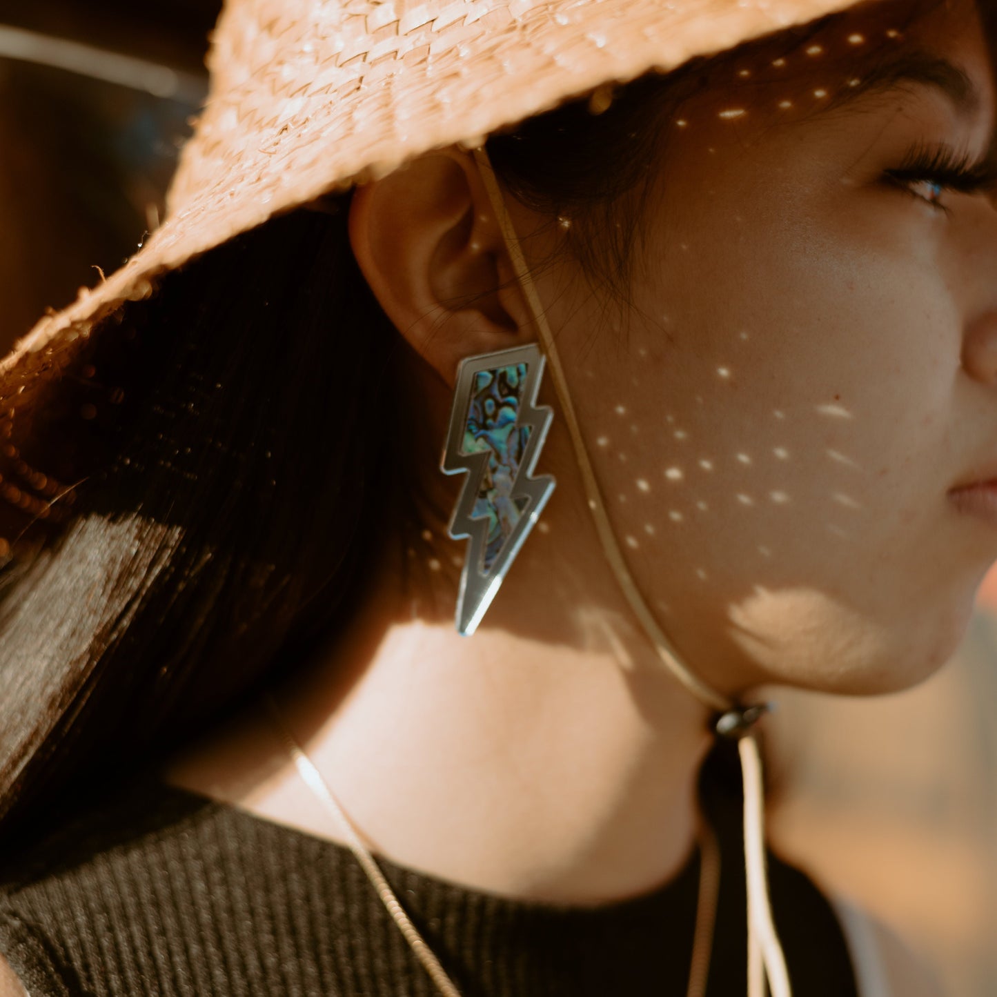 close up of acrylic silver lighting bolt earring with abalone inlay from copper canoe woman