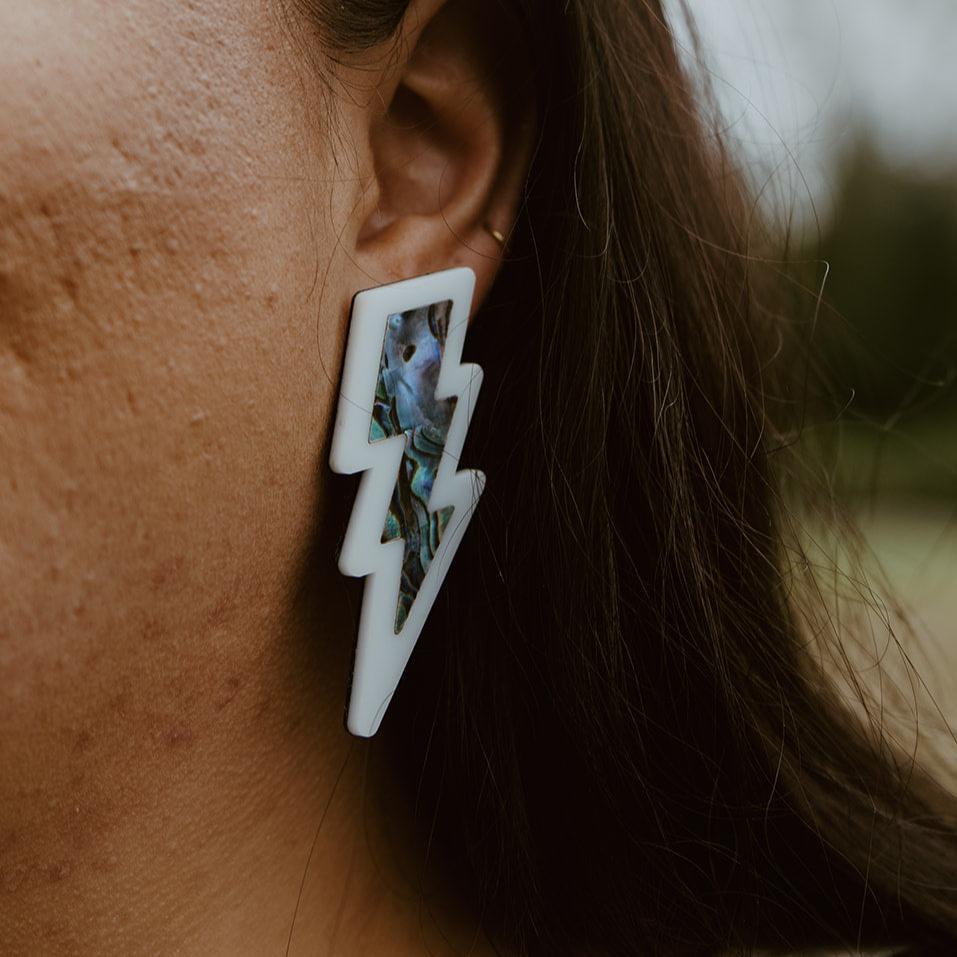 close up of white lightning bolt earring with abalone inlay from copper canoe woman