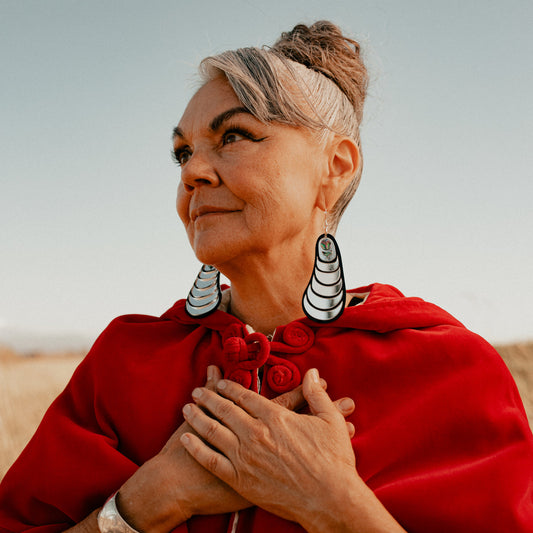 Model looks to the left with hands at their chest wearing the mussel-inspired earring "Coastal Strata" in silver by Copper Canoe Woman.