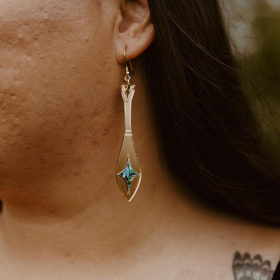 close up woman wearing gold mirror acrylic paddle earring with star abalone inlay from copper canoe woman