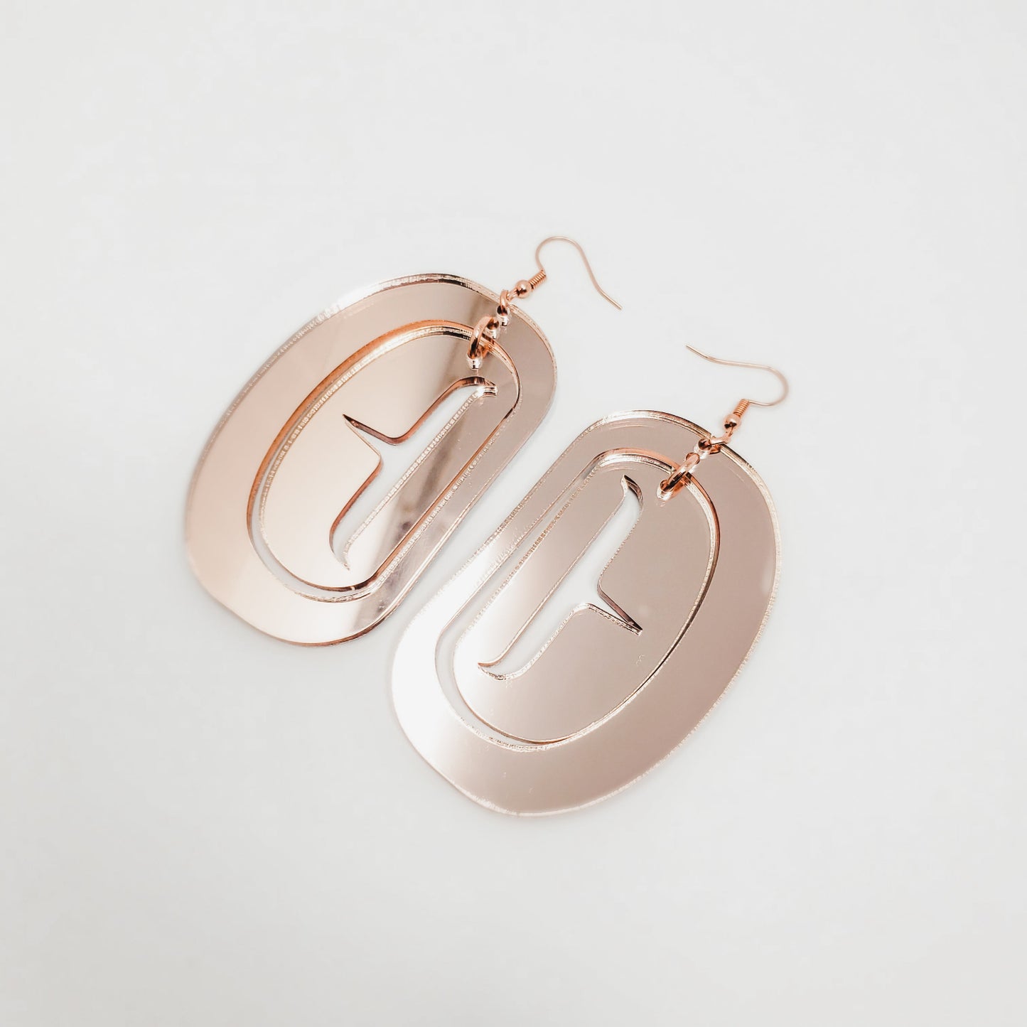 Large ovoid earrings in rose gold mirror acrylic with trigon cutout.