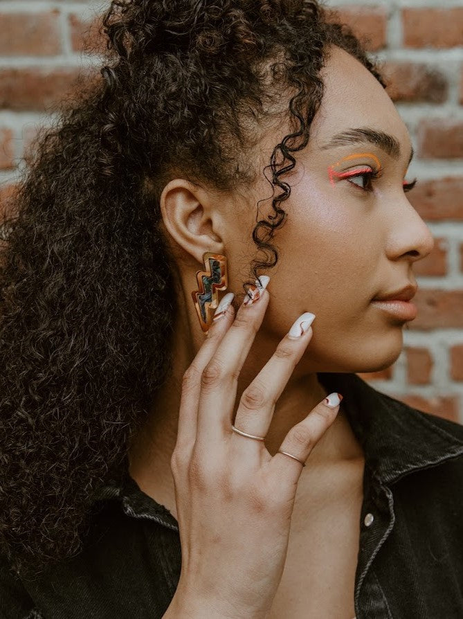 Model wearing the lightning bolt earring from Copper Canoe Woman in gold mirror acrylic with abalone inlay.