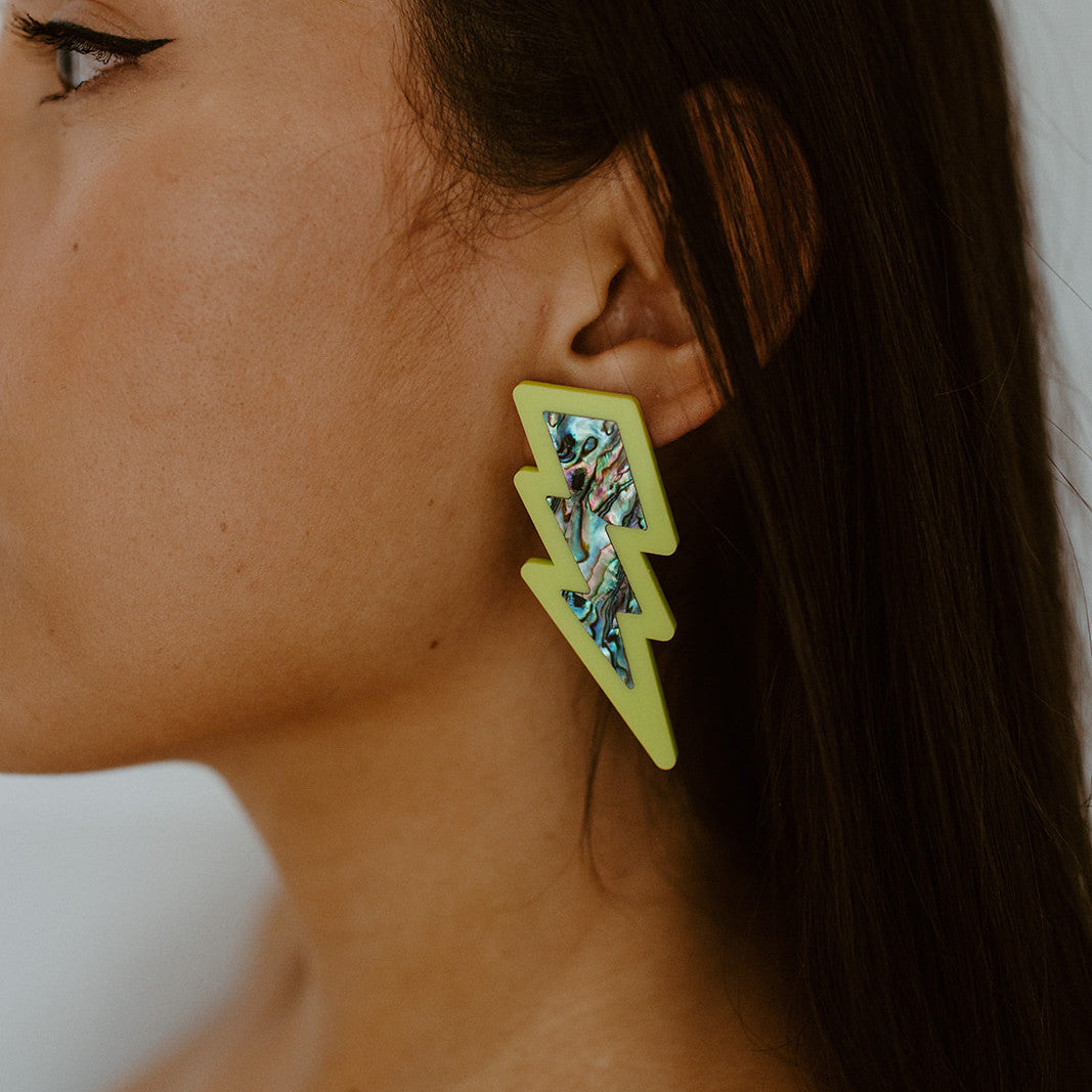 Closeup of model wearing neon pear acrylic lightning bolt earring with abalone inlay from Copper Canoe Woman.