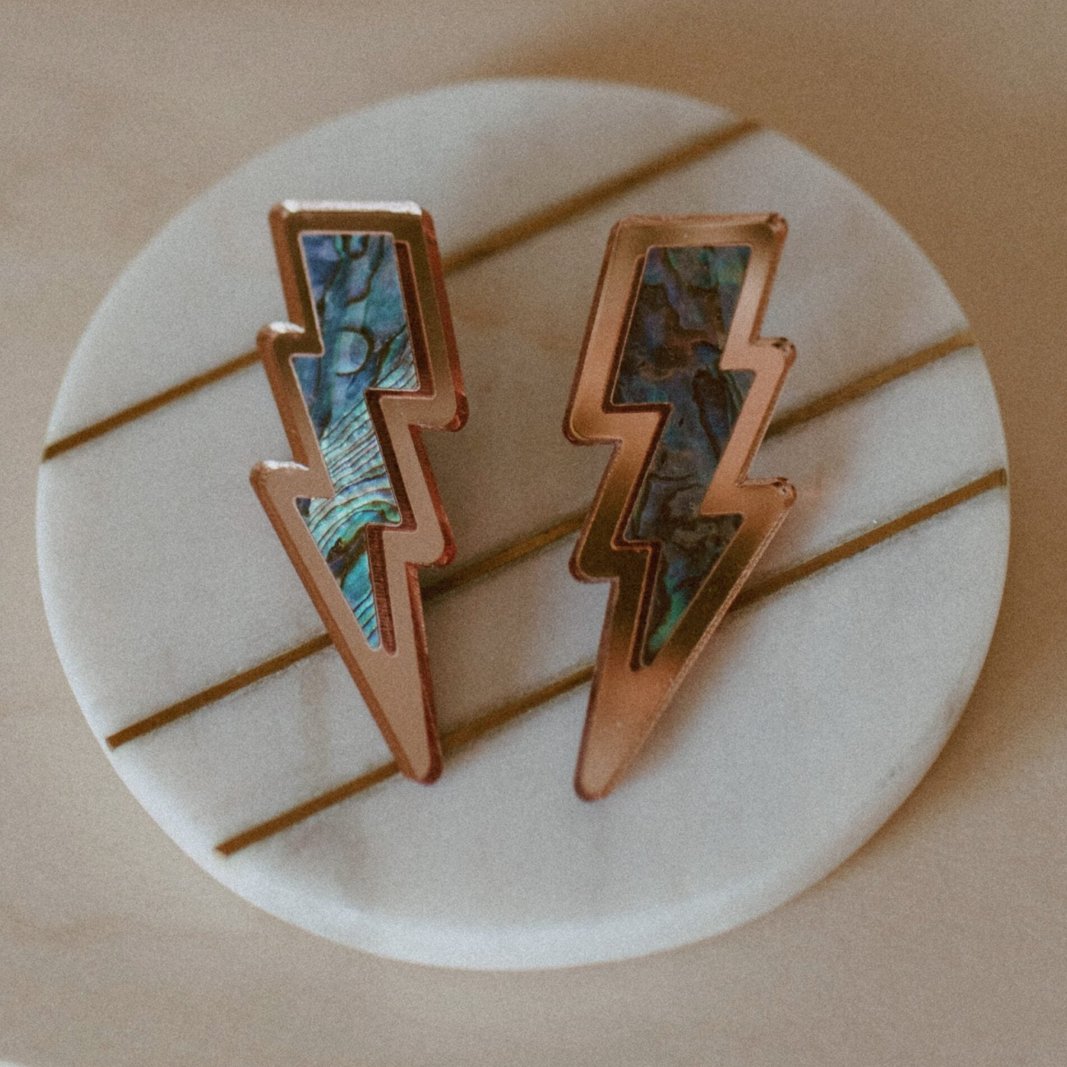 Lightning bolt earrings from Copper Canoe Woman in rose gold mirror acrylic with abalone inlay.