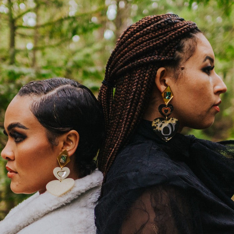 Models stand back to back wearing monochrome majesty earrings from Copper Canoe Woman.