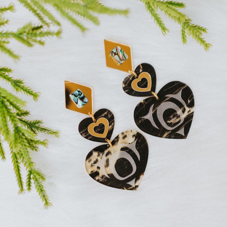 Closeup of a pair of monochrome majesty earrings from Copper Canoe Woman in obsidian gold acrylic.