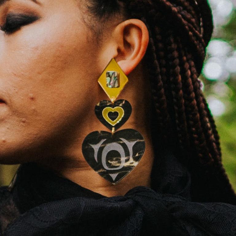 Model wearing monochrome majesty earring from Copper Canoe Woman in obsidian gold acrylic.