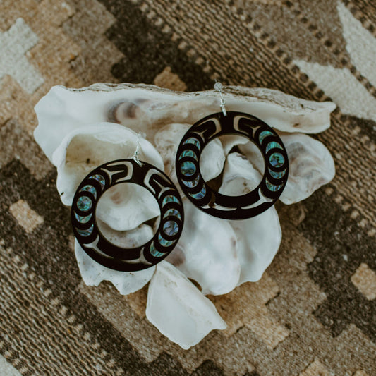 A pair of black Nala Hoop earrings from Copper Canoe Woman resting on a shell.