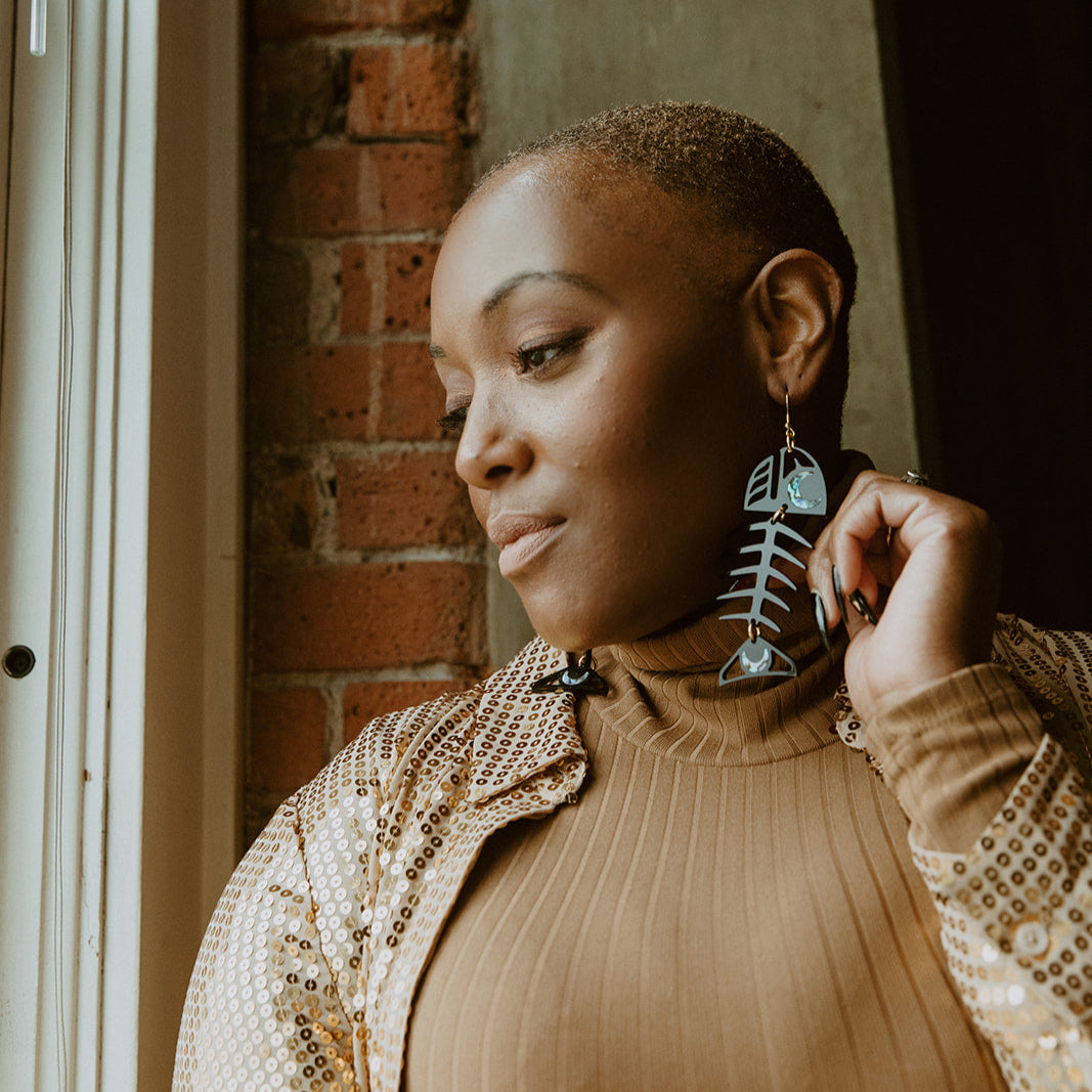 A person  looks out a window while wearing black acrylic Medium Salmon Ghost earrings from Copper Canoe Woman.