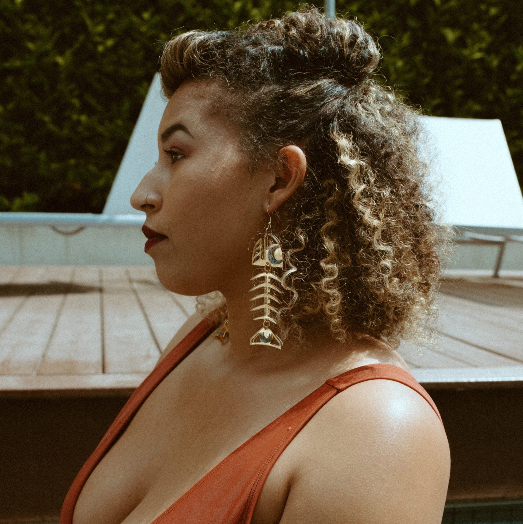 A model sits in profile by a pool while wearing gold mirror acrylic Medium Salmon Ghost earrings from Copper Canoe Woman.