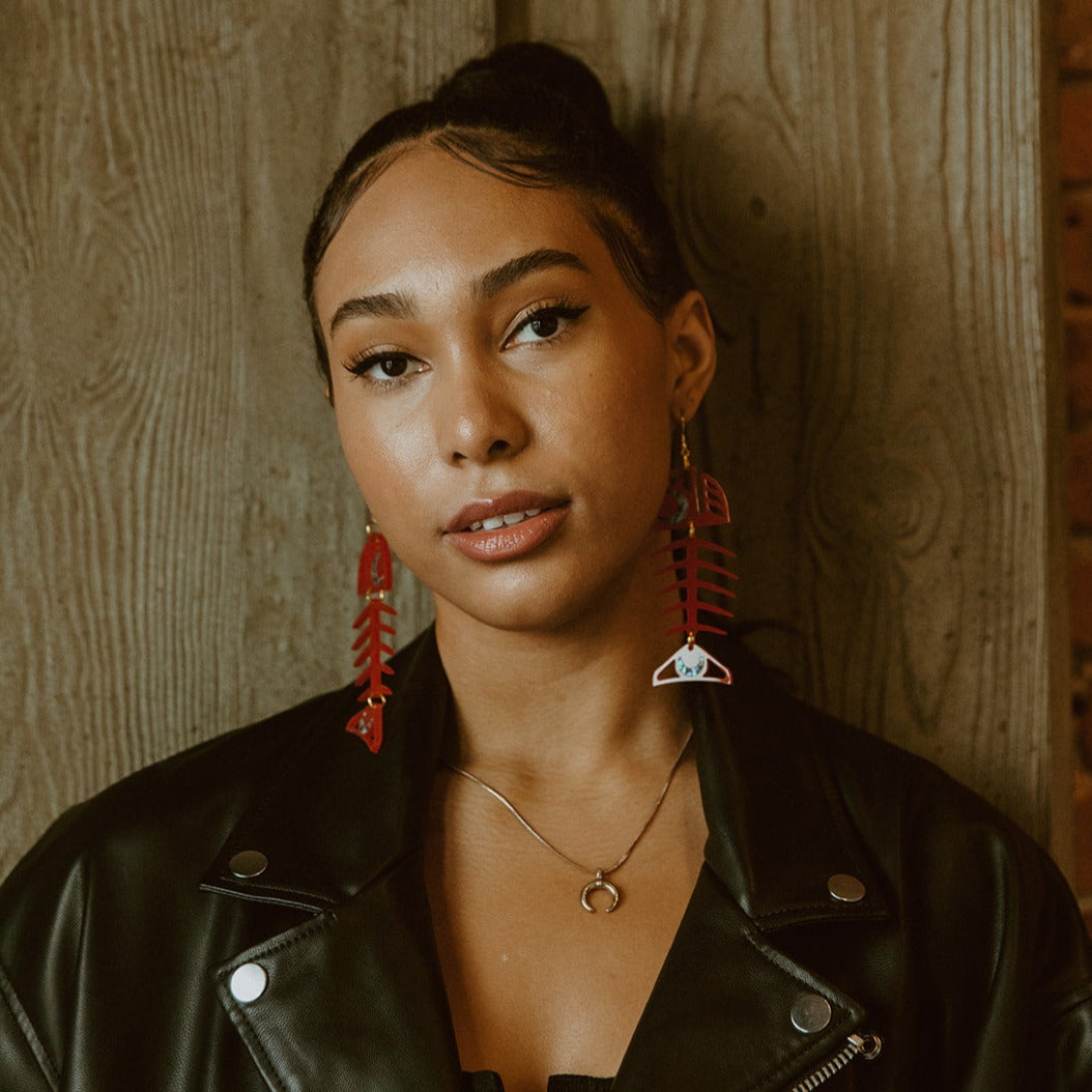 A model wearing red Medium Salmon Ghost earrings from Copper Canoe Woman stares into camera.