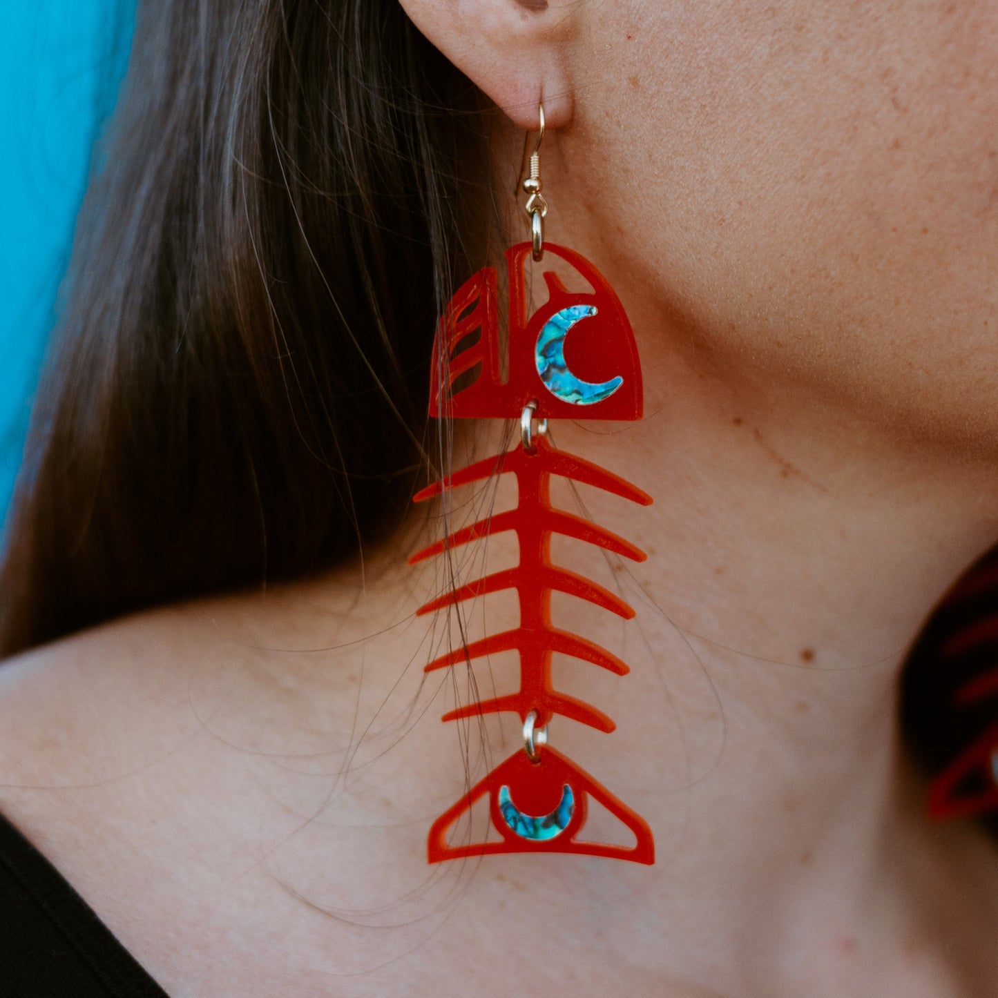 A Medium Salmon Ghost earring from Copper Canoe Woman in red acrylic worn by a model in closeup.