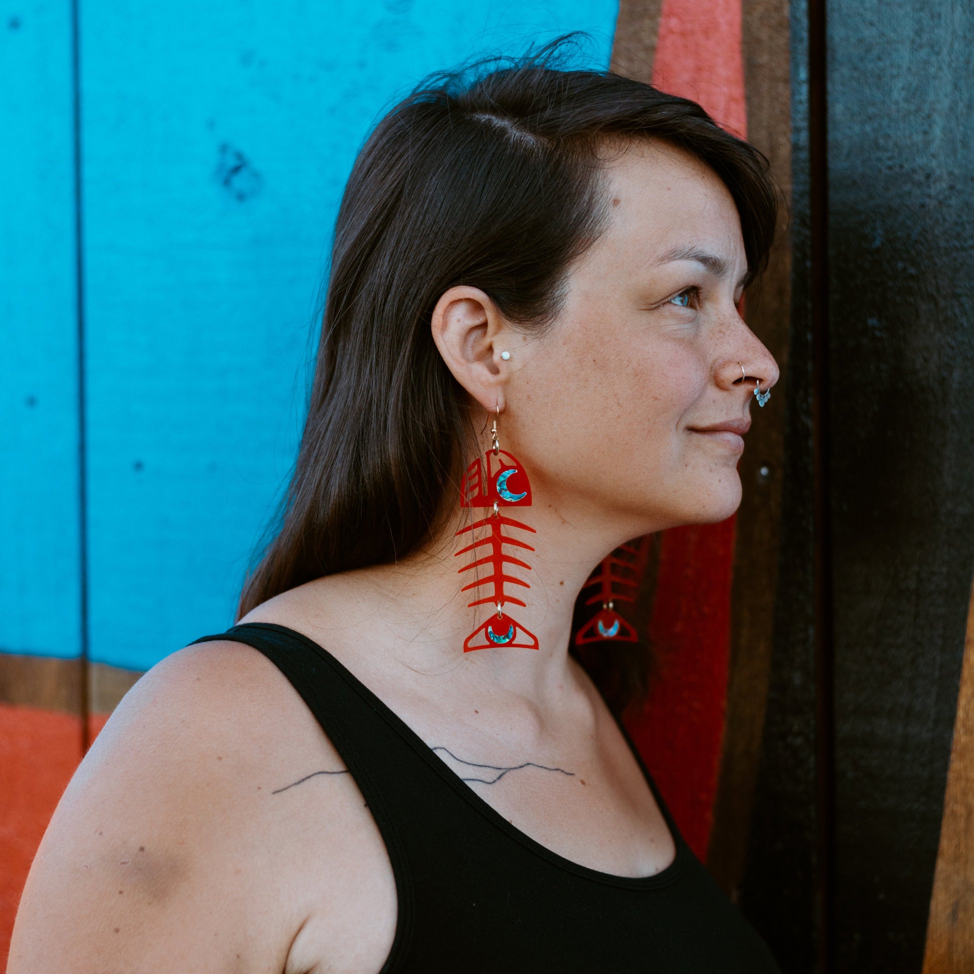 Model standing in profile wears a pair of Medium Salmon Ghost earrings in red acrylic from Copper Canoe Woman.