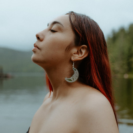 woman wearing silver acrylic crescent moon engraved with formline art from copper canoe woman