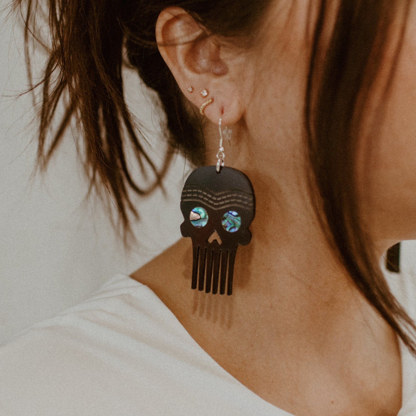 A model wears a pair of Skull Comb earrings from Copper Canoe Woman in chrome color acrylic.