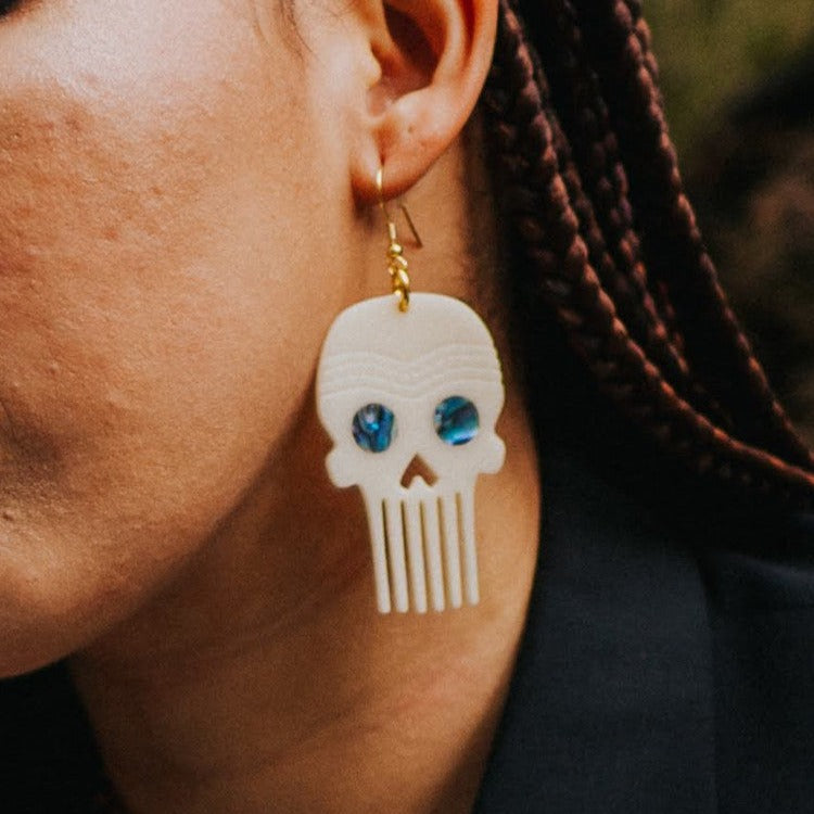 A closeup of a model wearing the Skull Comb earring in ivory acrylic from Copper Canoe Woman.