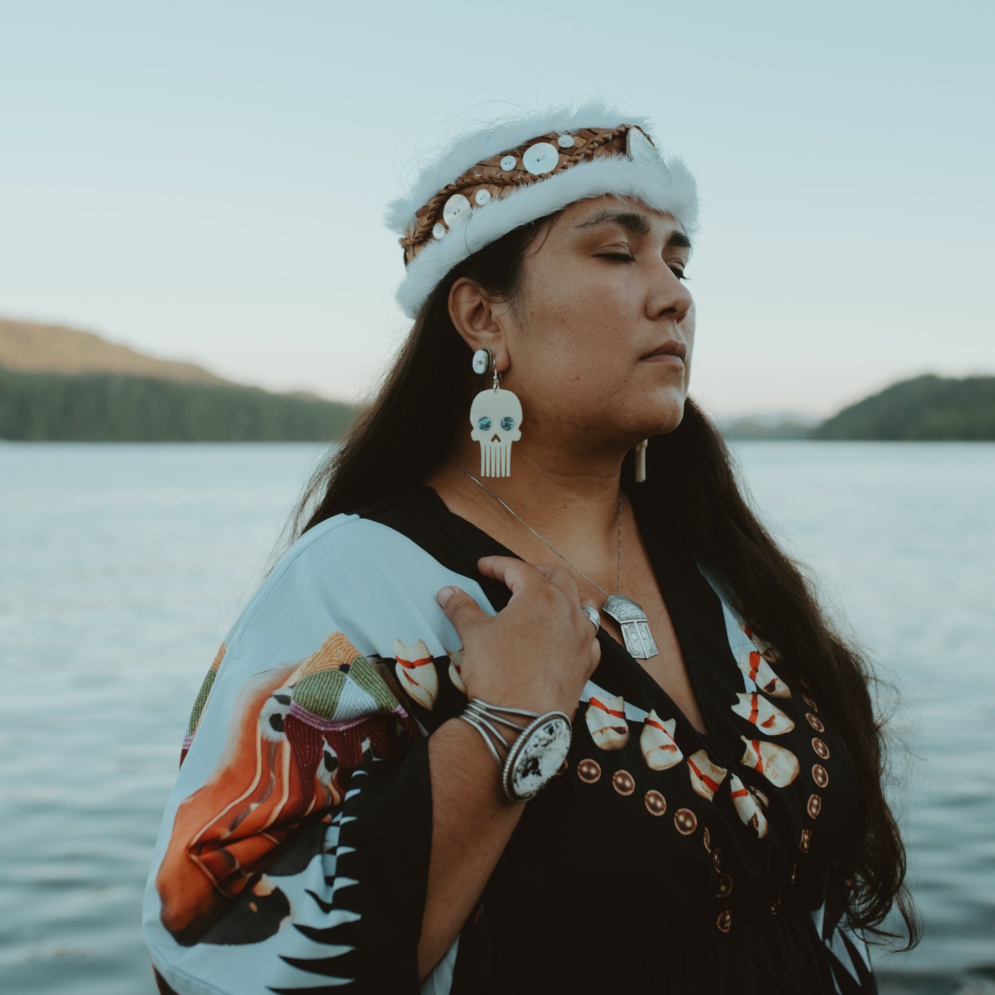 A woman stands in water wearing the Skull Comb earing in ivory acrylic from Copper Canoe Woman.