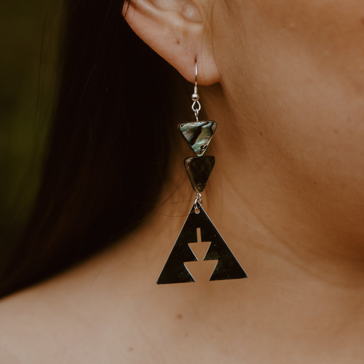 close up of woman wearing sterling silver triangle with southwest geometric shapes topped with two abalone triangle beads from copper canoe woman