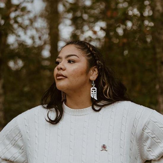 woman wearing Sterling Silver earrings of wings in formline art: one eagle, one raven. Topped with triangle abalone beads from copper canoe woman