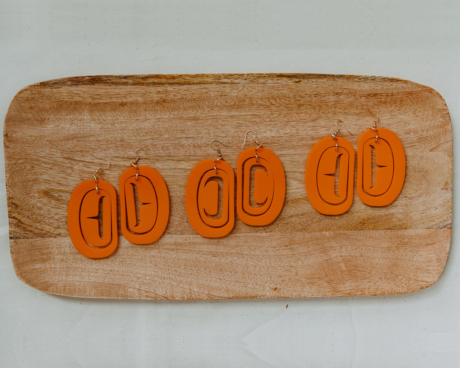 Three pairs of orange ovoid hook earrings on a slab of wood