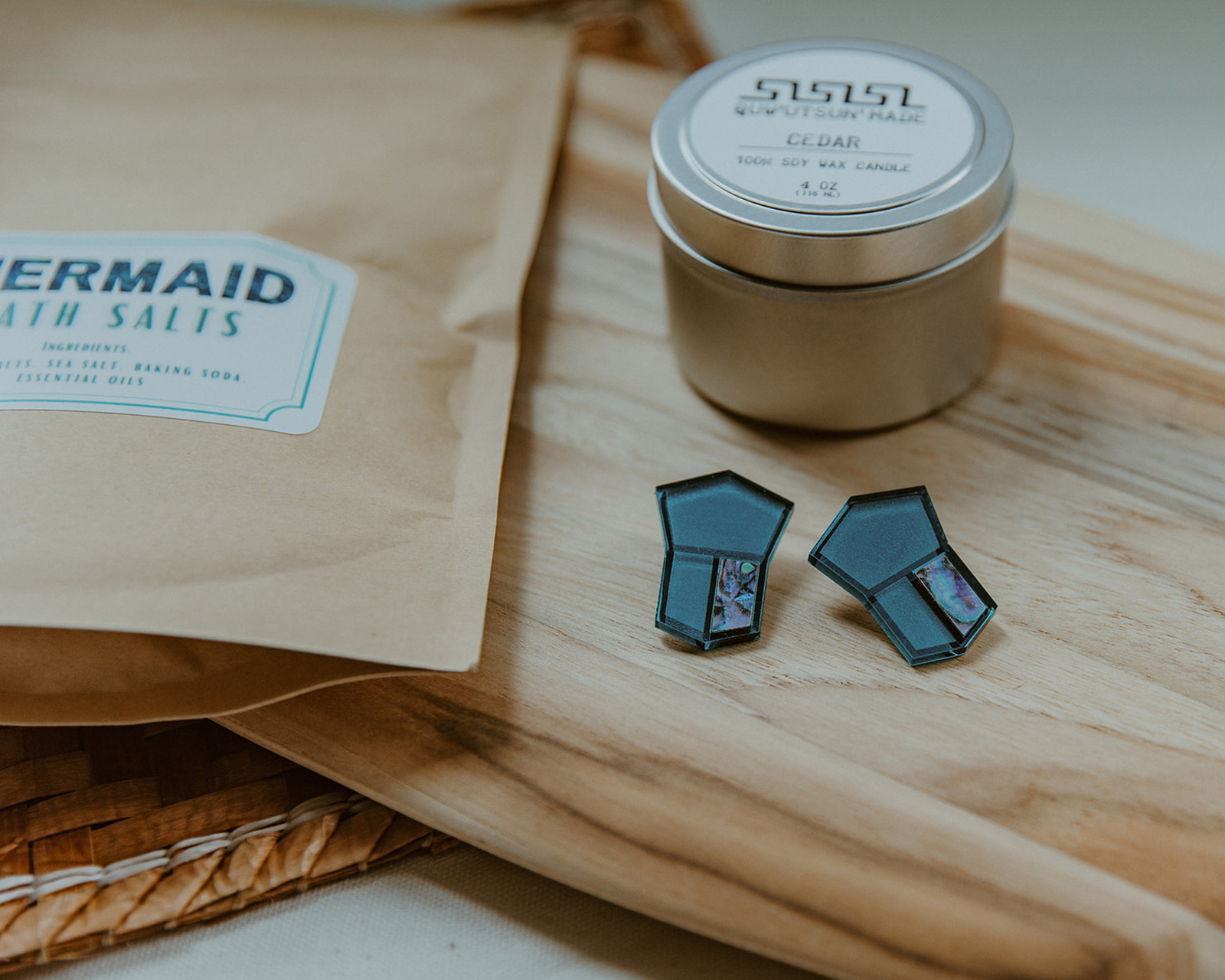 A cedar wax candle, manila bag of bath salts, and geometric blue and abalone post earrings