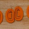 Orange ovoid formline earing on hooks with crescent cutout.
