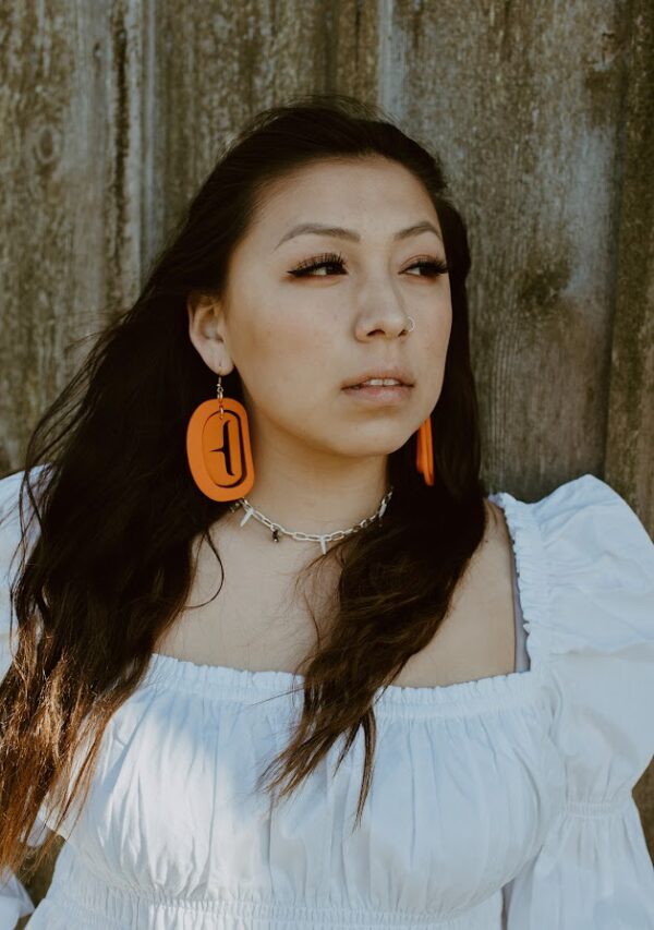 Indigenous model wears orange trigon ovoid formline earrings.