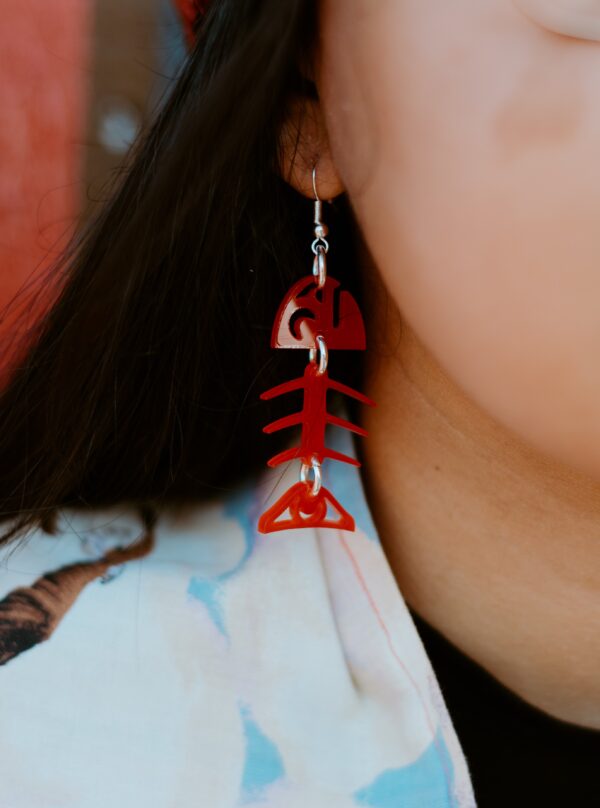 Model wearing small salmon bone earring in red acrylic.