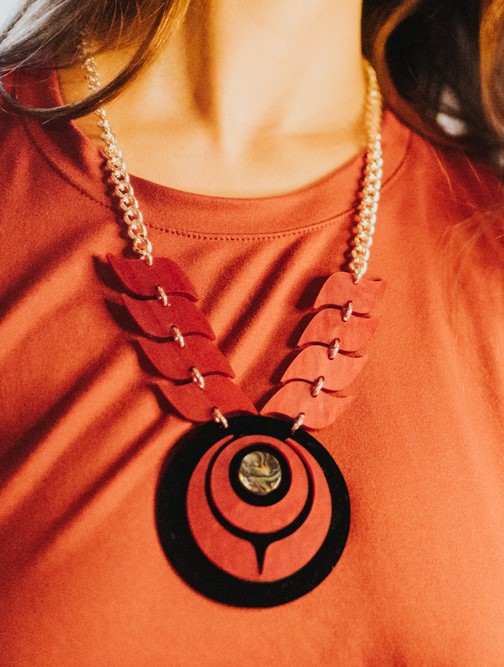 Model wearing owl eye style necklace in red on black acrylic.