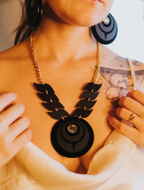 Model wearing owl eye style necklace in black on black acrylic.