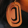 Close up of large ovoid earring in cedar wood with a crescent cutout.