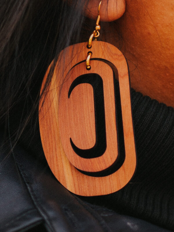 Close up of large ovoid earring in cedar wood with a crescent cutout.