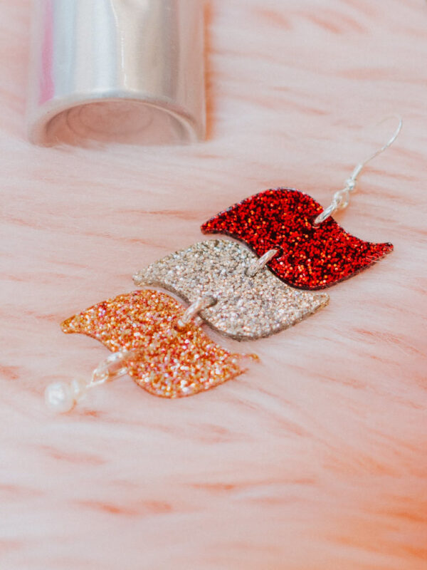 3-tier s-shape acrylic 'Drop of Love' earring in three glitter colors laying on pink fur.